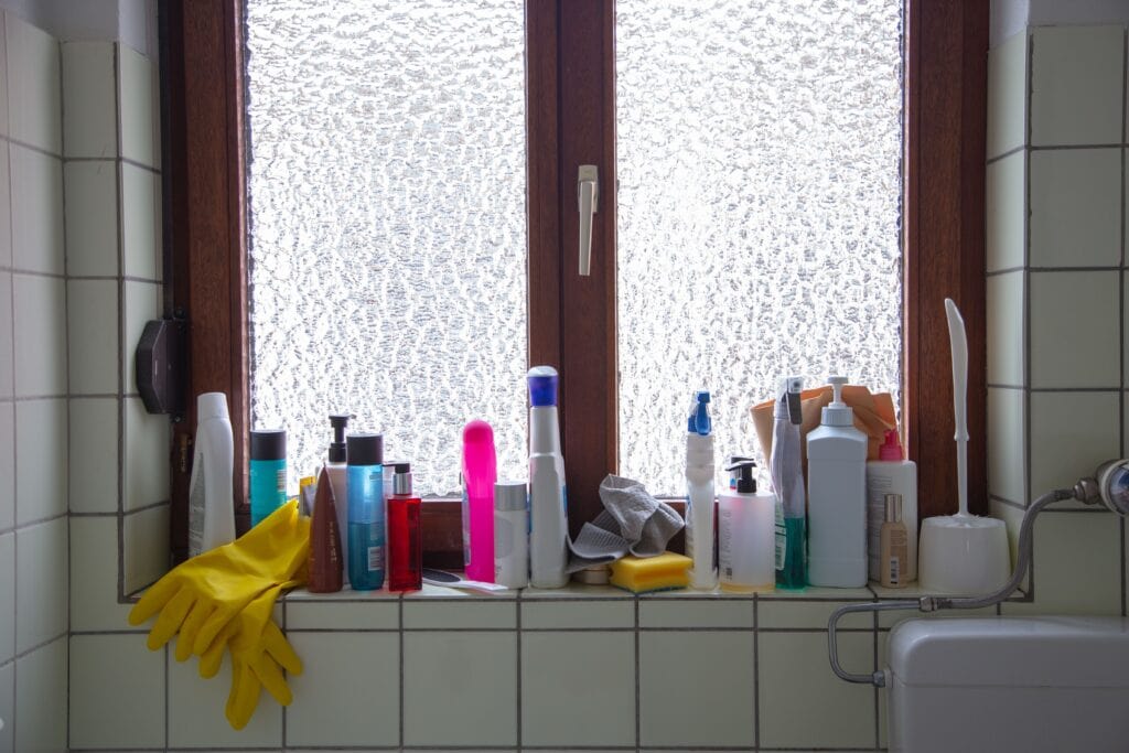 cluttered bathroom window with bath and cleaning supplies on window ledge with two windows having simulated ice pattern frost window film installed