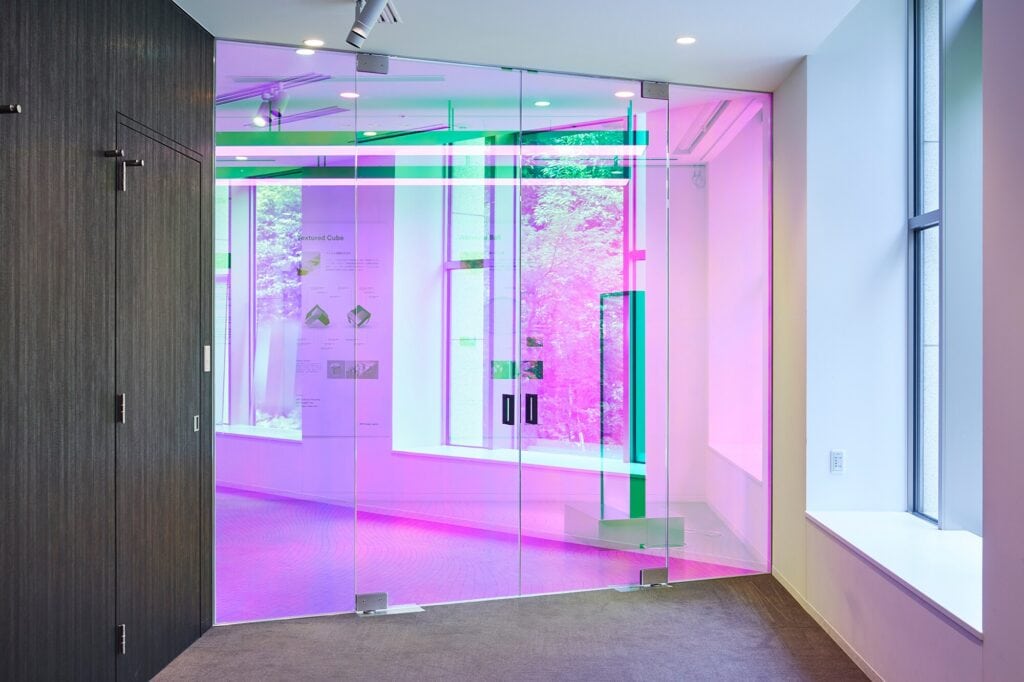 Glass doors in a modern commercial hallway, bathed in pink and purple lighting with a dark wood wall on the left.
