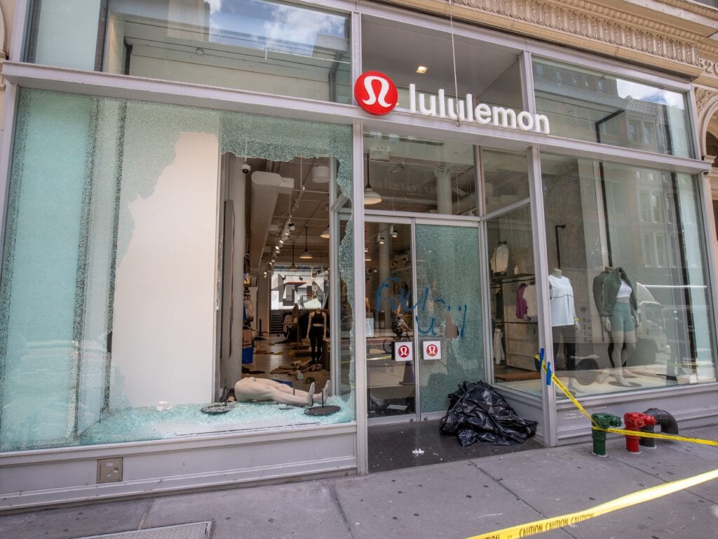 Smashed retail storefront window with a large hole in the shattered glass and no security film, leaving the store wide open to forced entry.