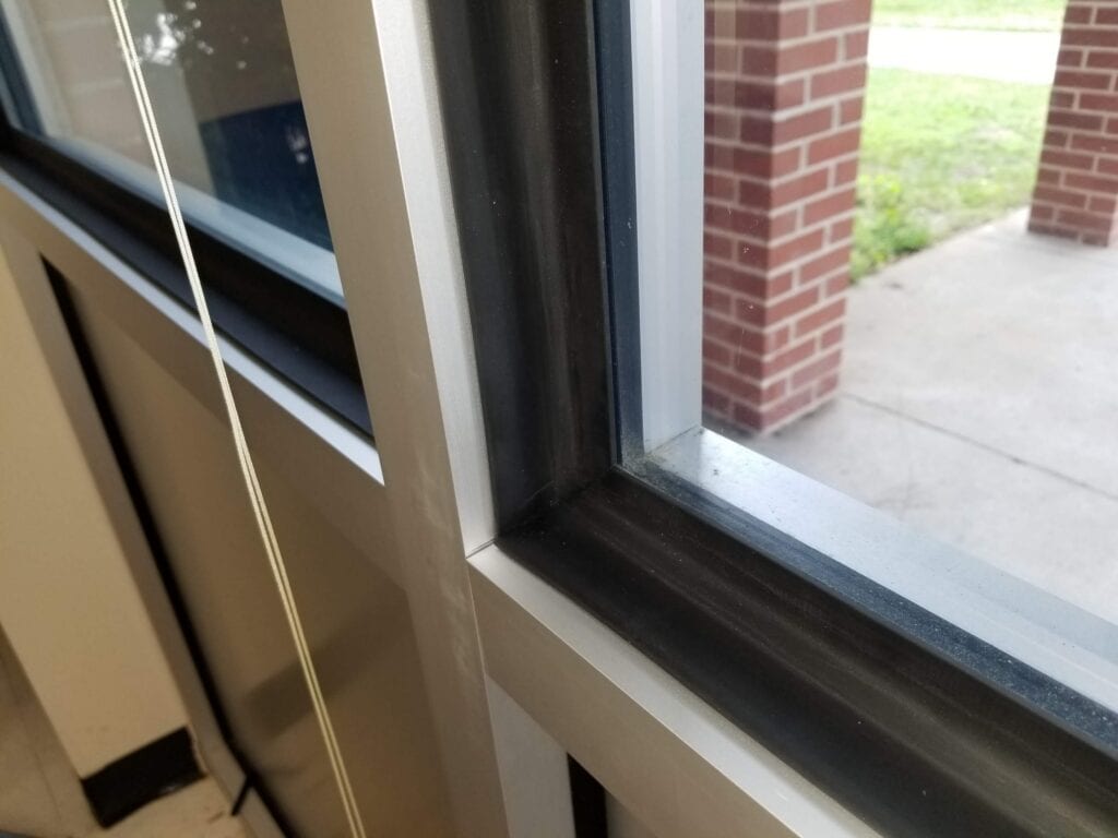 Closeup image of a black rubber molding installed on the frame edge of a commercial type window unit with a silver metal frame.